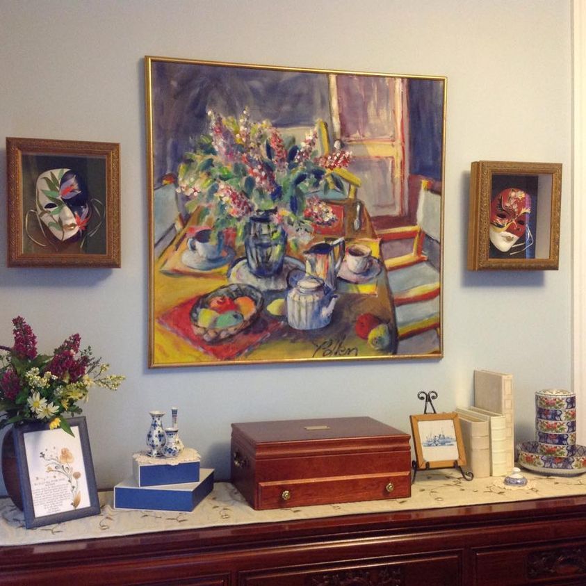 A cozy room with framed portraits and a colorful floral painting above a wooden sideboard.